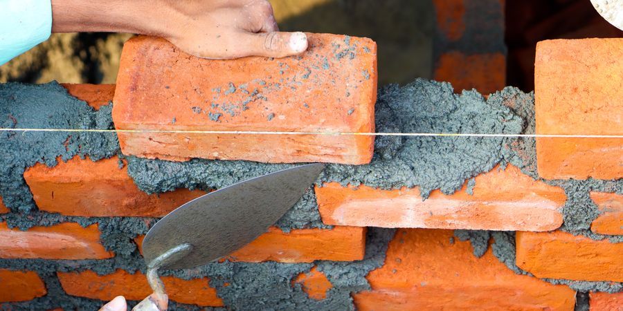 Worker laying bricks with precise mortar joints — the same technique principles apply to industrial refractory brick installation