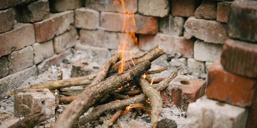 Small campfire flickering within a rustic brick enclosure outdoors — proper firebricks handle this thermal cycling without cracking