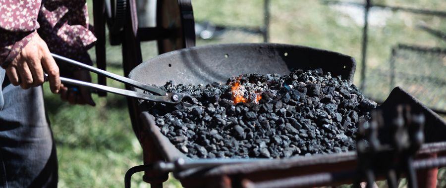 Blacksmith using tongs beside an outdoor solid-fuel forge