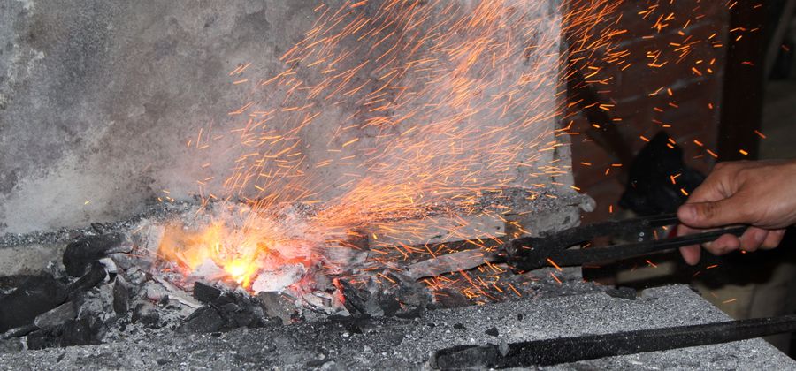 Blacksmith working at a forge with sparks flying while refractory lining requirements are evaluated