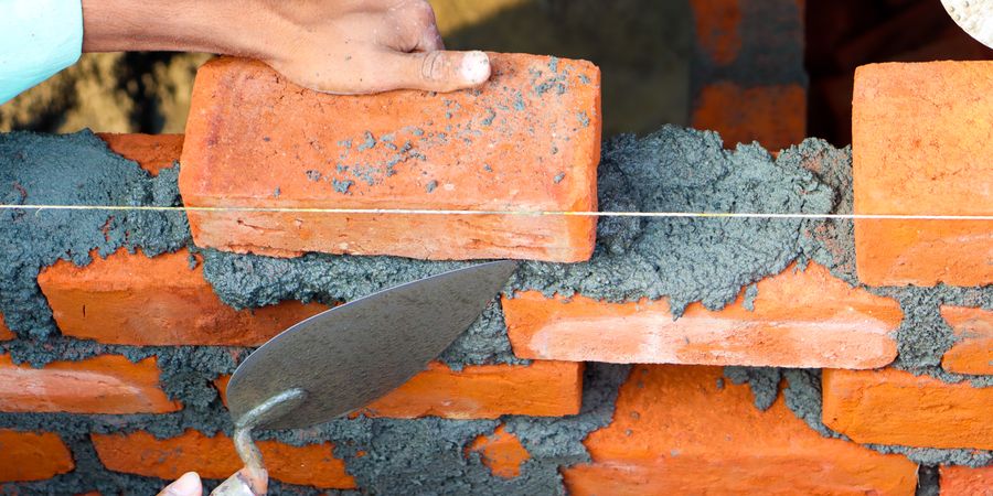 Worker laying bricks with precise mortar joints — the same technique principles apply to industrial refractory brick installation