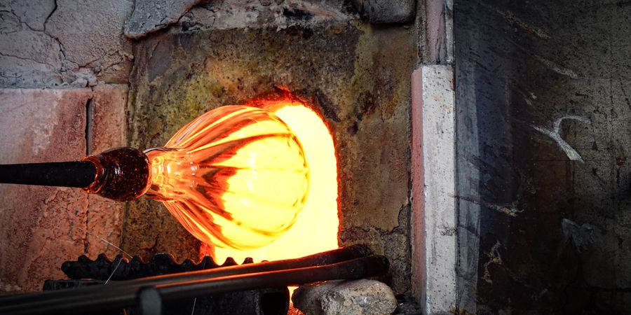 Close-up of glowing glass being shaped in a fiery glassblowing furnace, showing the intense heat and liquid glass that refractory bricks must contain