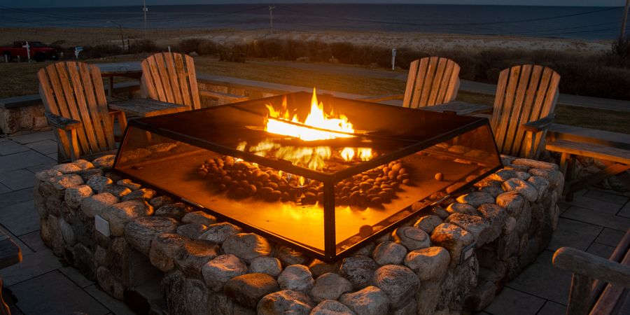 Glowing fire pit surrounded by chairs near a beach — outdoor fireplaces and fire pits demand proper firebrick linings to survive regular use