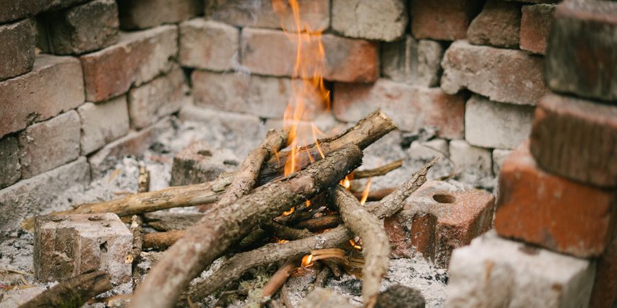 Small campfire flickering within a rustic brick enclosure outdoors — proper firebricks handle this thermal cycling without cracking