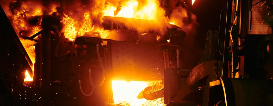 Industrial furnace with bright flames and heavy machinery — insulating brick backup layers keep the outer structure safe