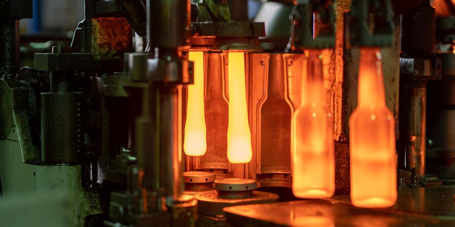 Close-up of molten glass bottles being shaped in a factory machine, showing the end-product quality that depends on correct glass furnace refractory selection