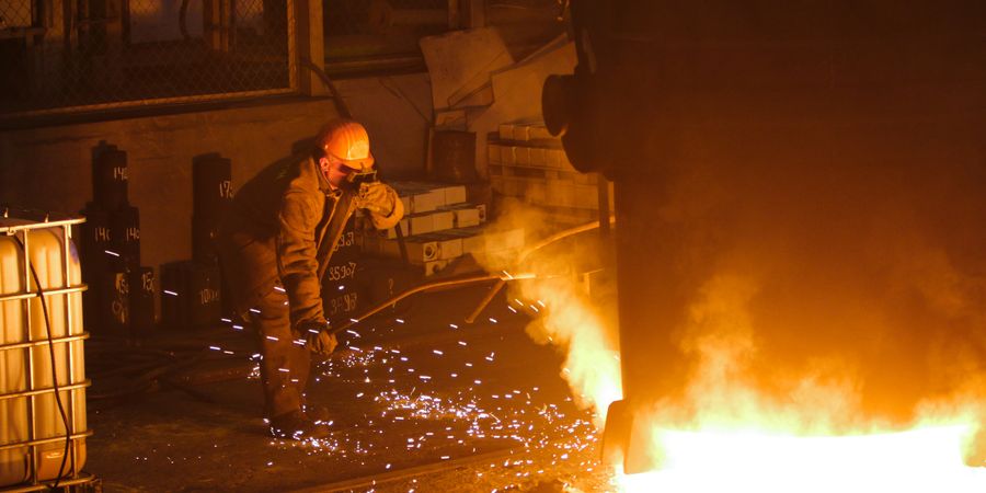 Steelworker in protective gear working near molten metal in an industrial foundry — the environment in which refractory lining performance is proven
