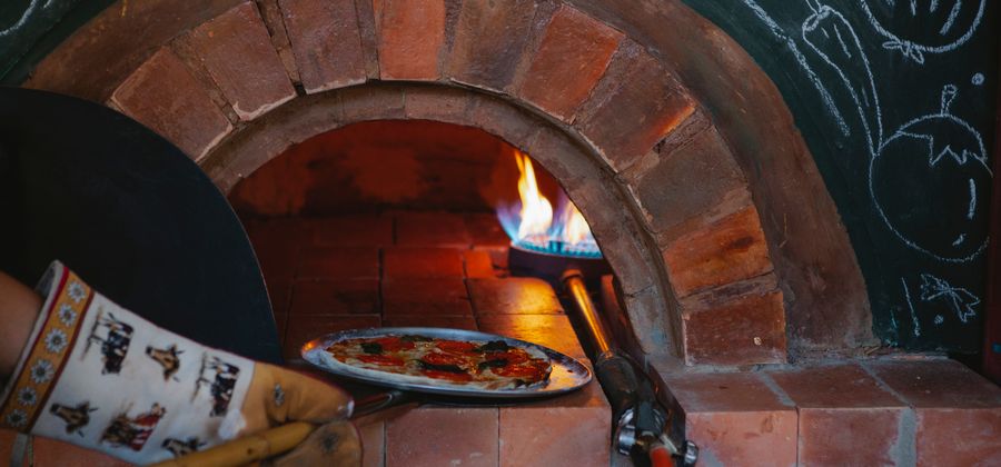 Delicious pizza baking in a traditional wood-fired refractory brick oven — the firebrick floor and dome maintain the intense heat that makes Neapolitan-style pizza possible